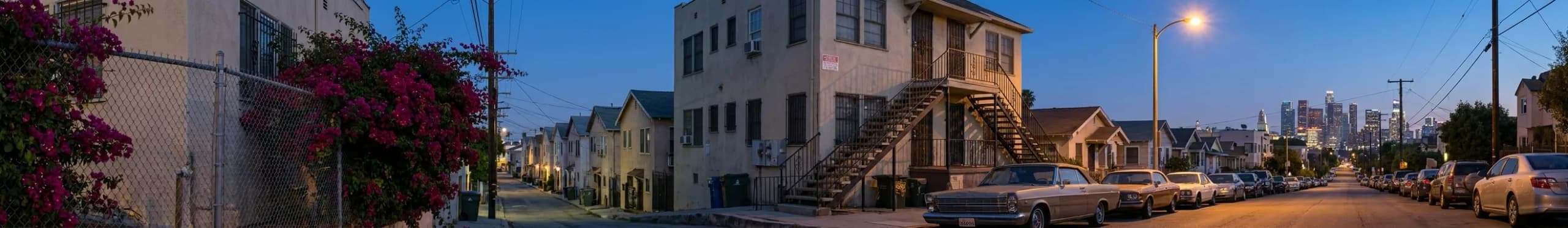 An Echo Park side street on a warm evening, cars parked nose-to-tail along a steep road past stucco bungalows and bougainvillea, with the lit downtown skyline small at the bottom of the hill