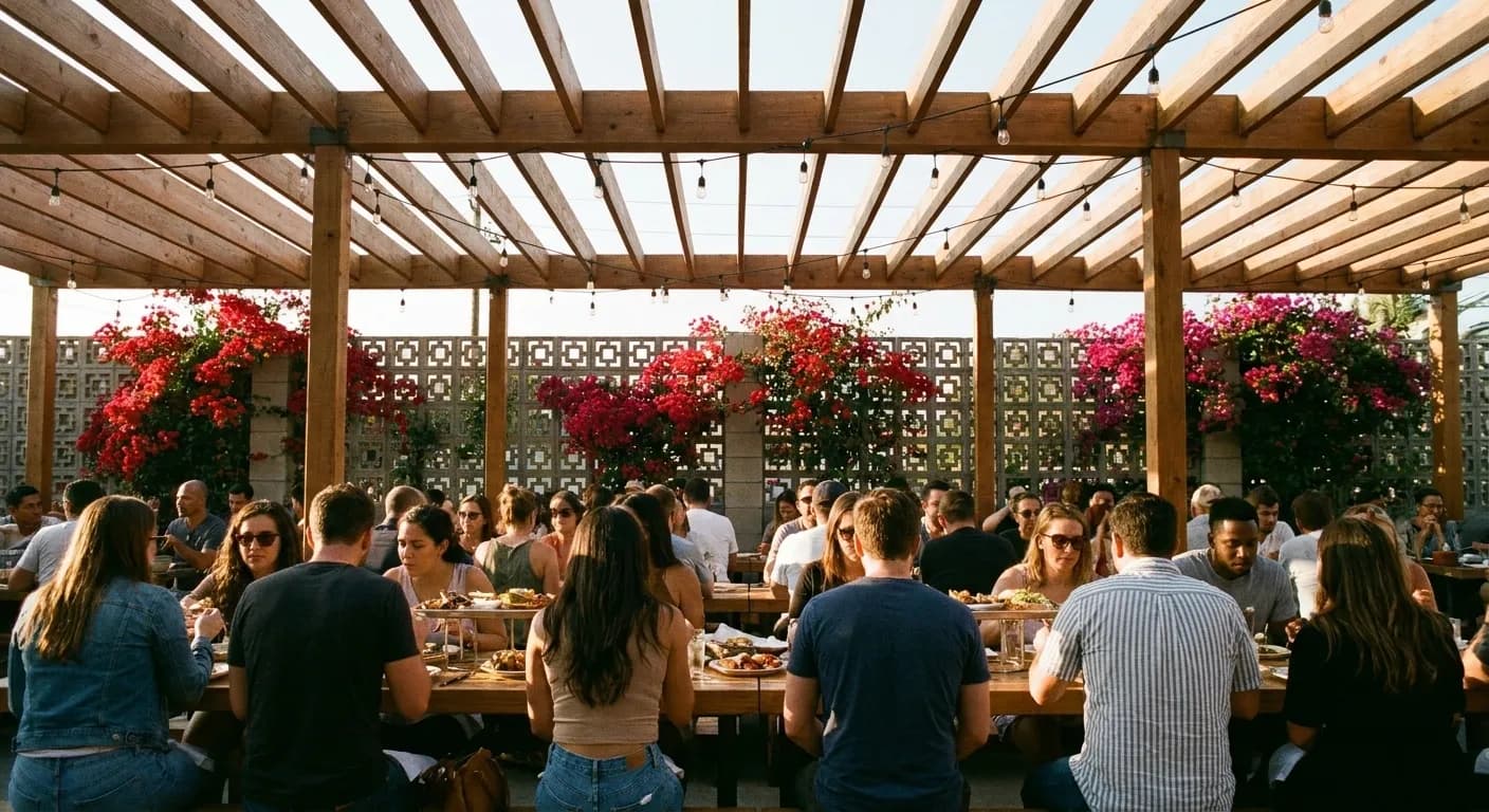 A large Los Angeles restaurant patio under a slatted pergola, with long communal tables of seated groups and shared platters down the centre