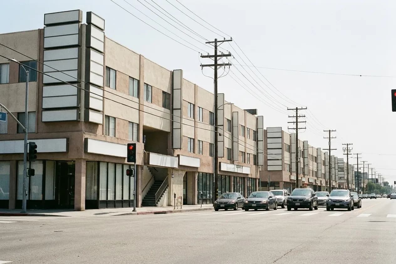 A Koreatown boulevard in Los Angeles by day, blank sign panels stacked up each building corner above a narrow stairwell entrance
