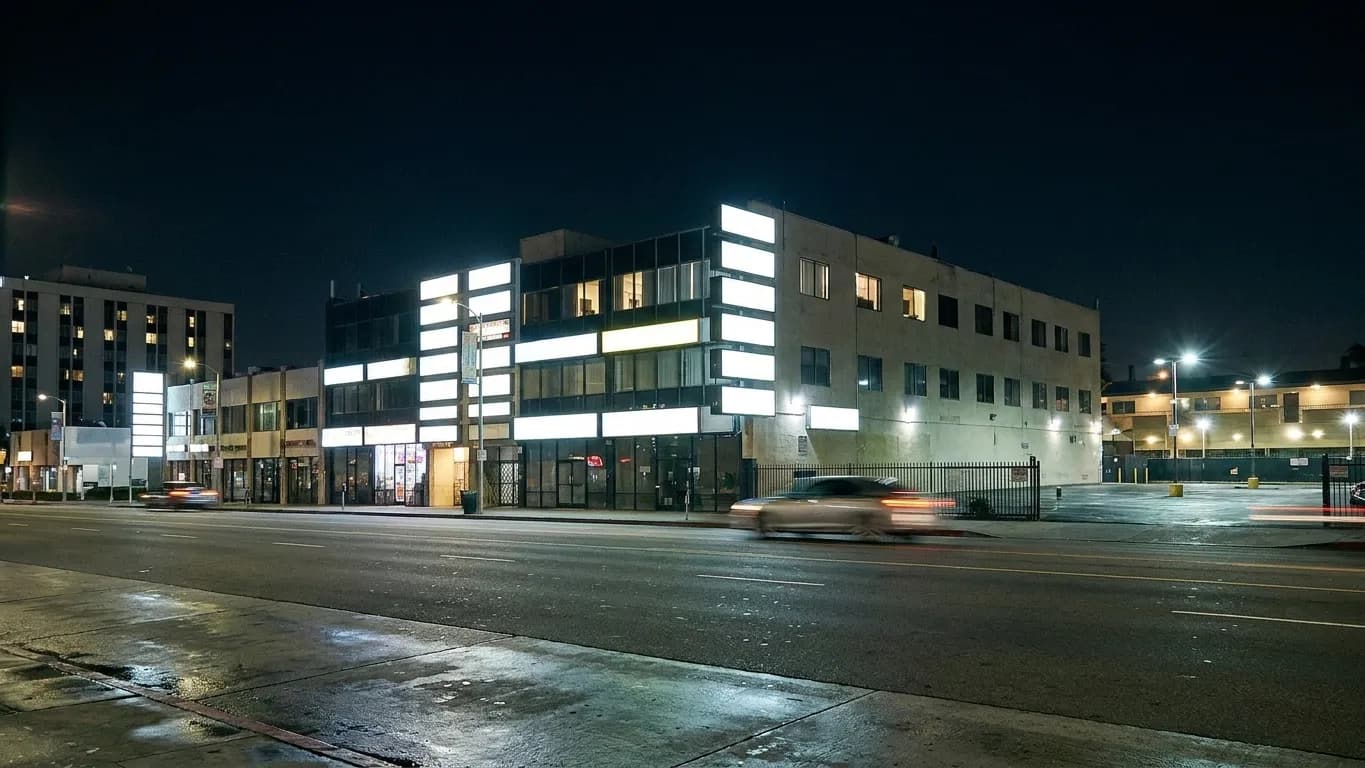 A Koreatown boulevard in Los Angeles at 1am with lit upper-floor windows, blank illuminated sign panels and an empty road