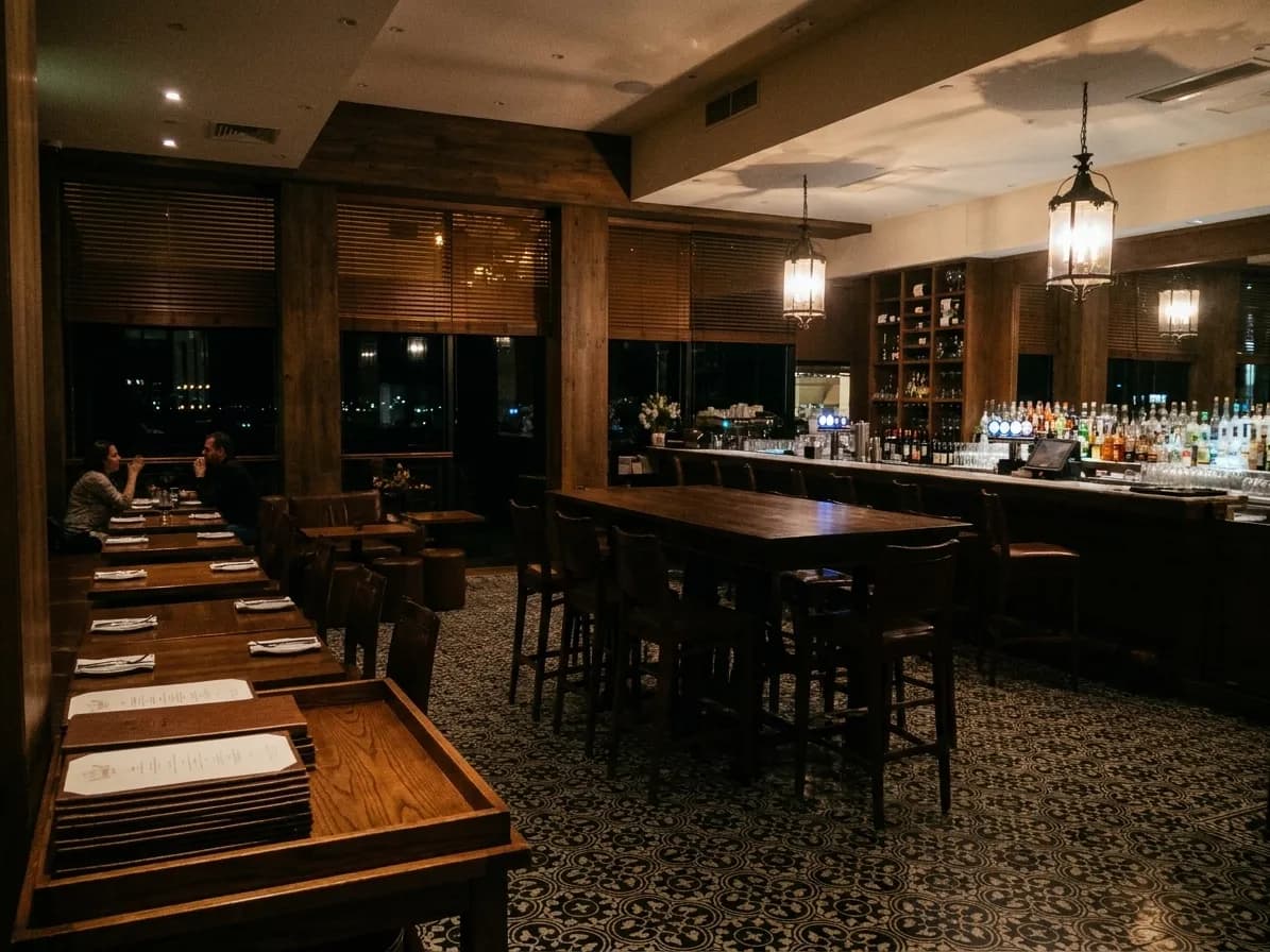 A Los Angeles dining room near midnight with a few occupied tables at the far end, a lit back bar and black windows behind half-drawn blinds