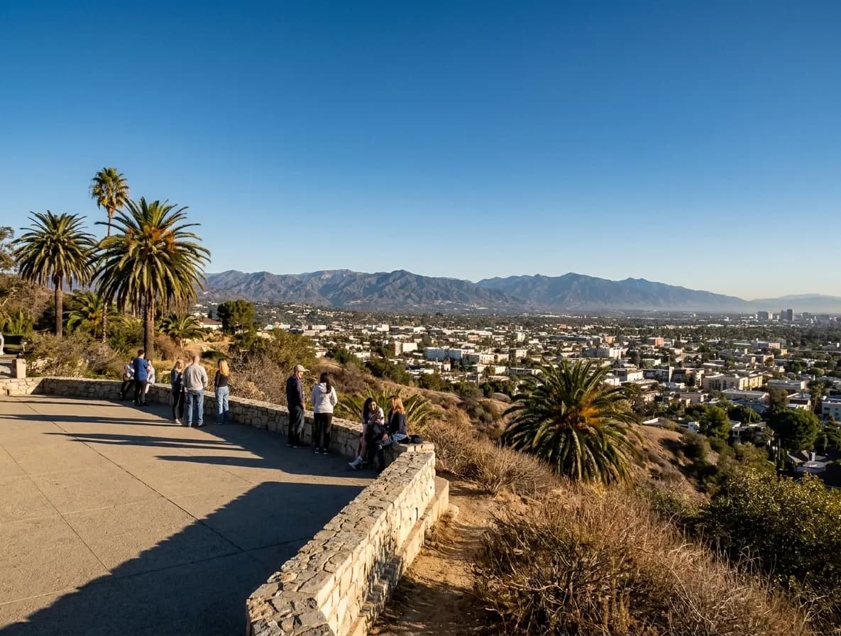 A hillside park overlook in Los Angeles on a clear morning, people at a low wall above a wide basin of city stretching to distant mountains