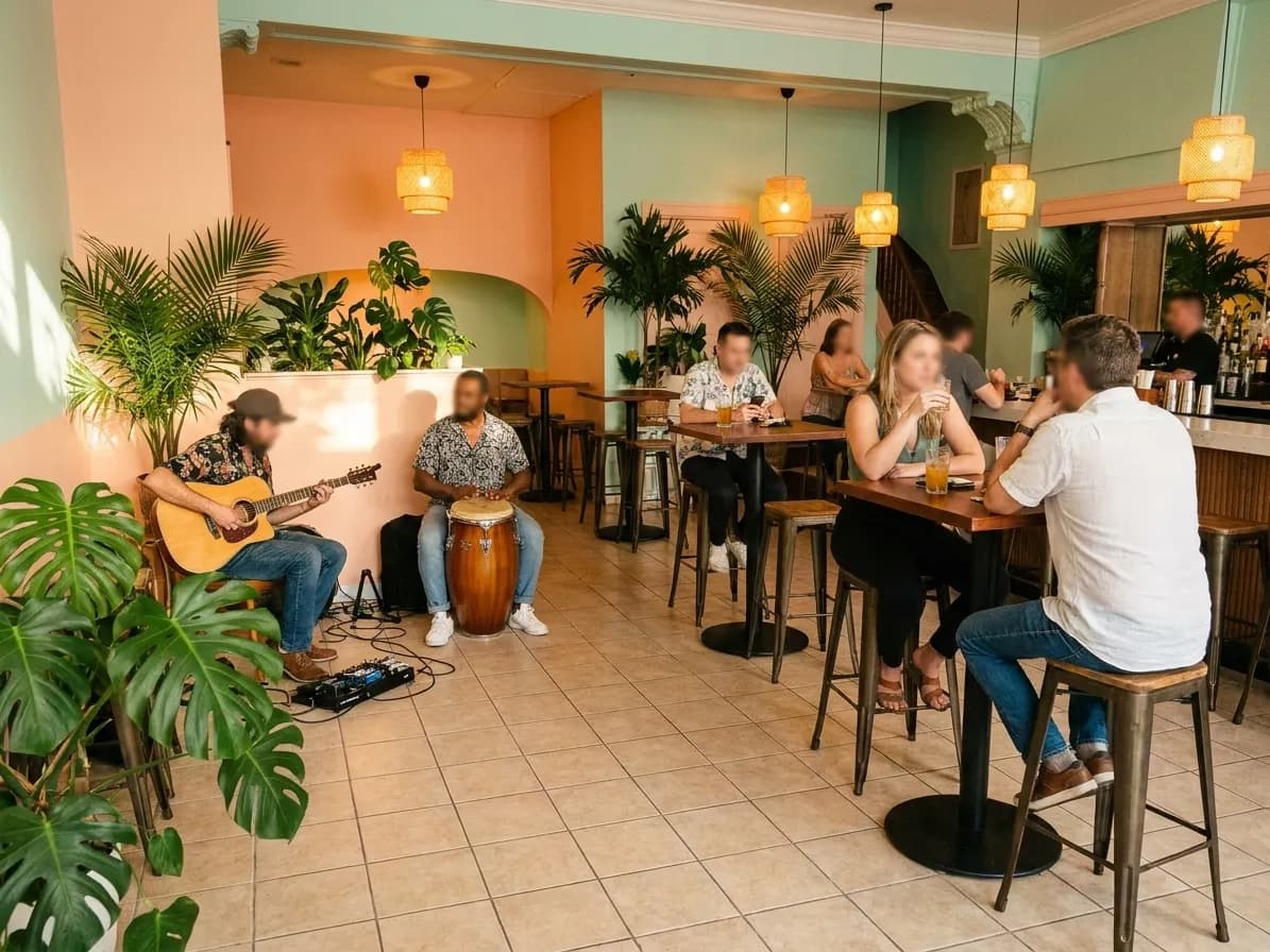 A Miami bar with a guitarist and percussionist playing in the corner on a tiled floor beside drinkers at high tables and a pastel wall