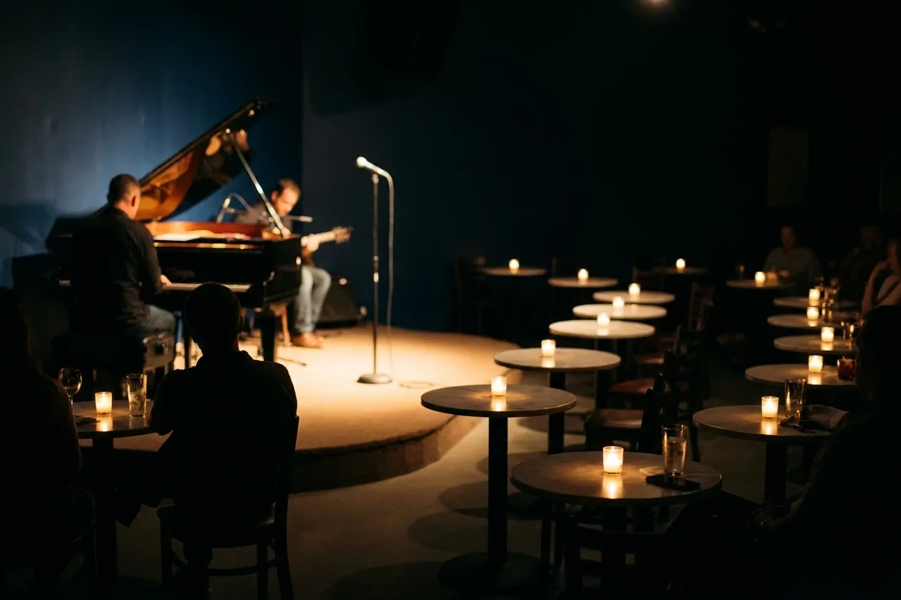 An intimate Miami listening room with twelve small candlelit tables and a low stage holding a piano and a single microphone