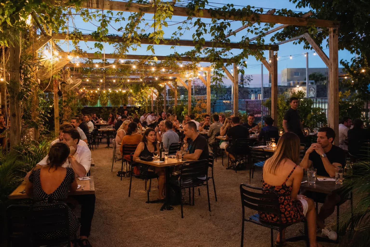 A bustling outdoor courtyard patio at Barcelona Wine Bar in Miami, filled with patrons enjoying tapas and glasses of Spanish wine under warm string lights.