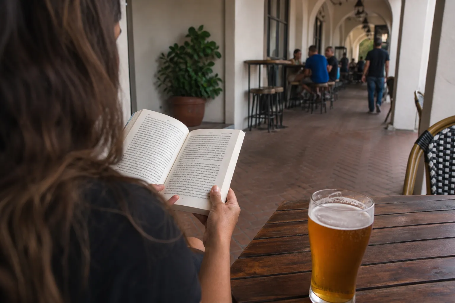 A person reading a book with a pint of beer on a patio in Coral Gables.