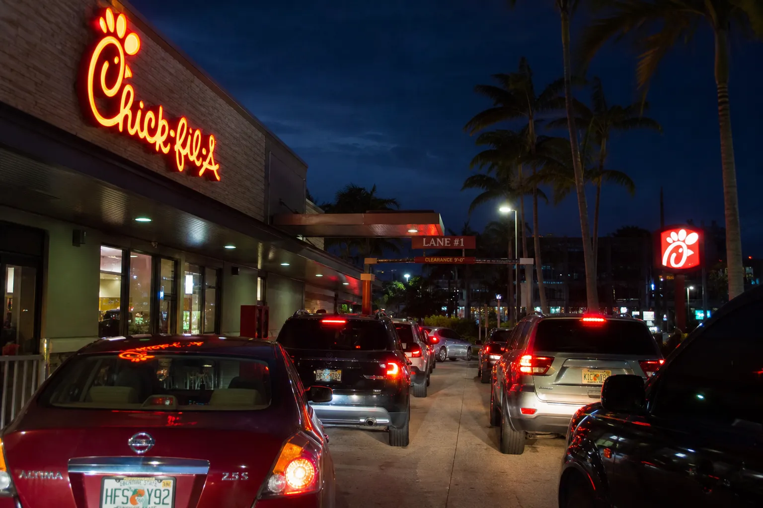 Bright neon lights and palm trees at the Pinecrest Chick-fil-A location along US-1 at night.