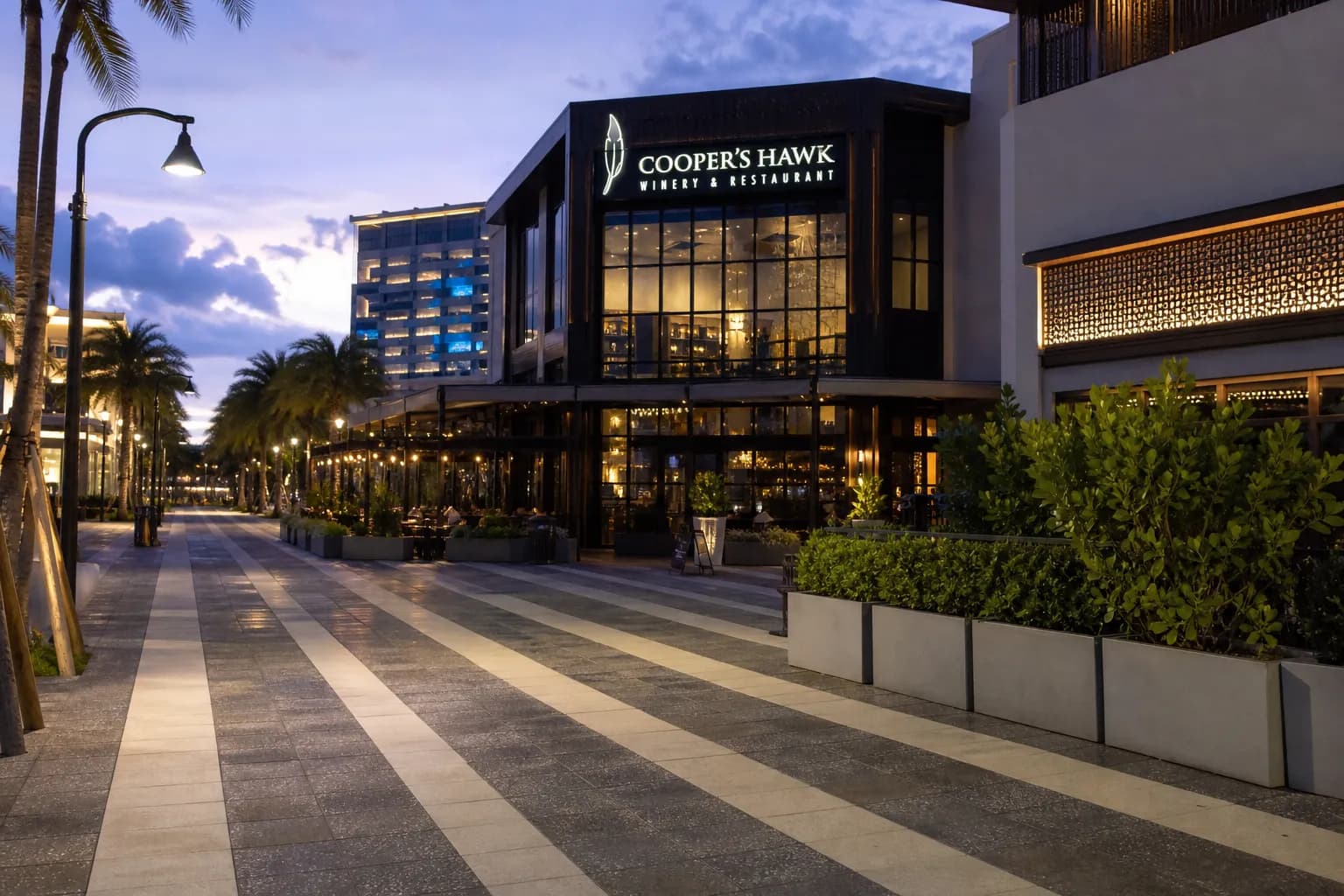 The modern exterior entrance of Cooper's Hawk at CityPlace Doral illuminated at dusk.
