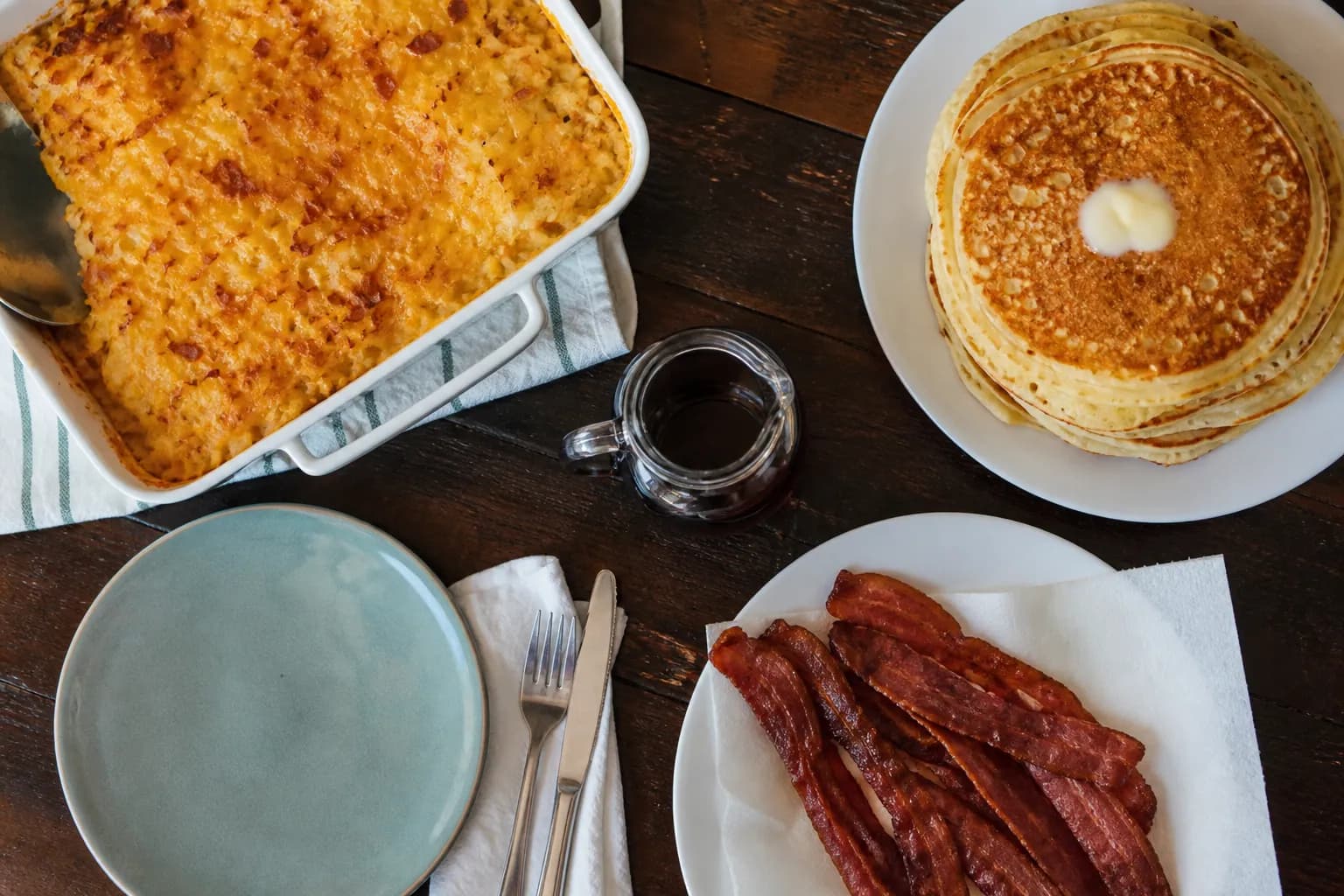 A hearty country breakfast spread with pancakes, bacon, and hashbrown casserole on a wooden table