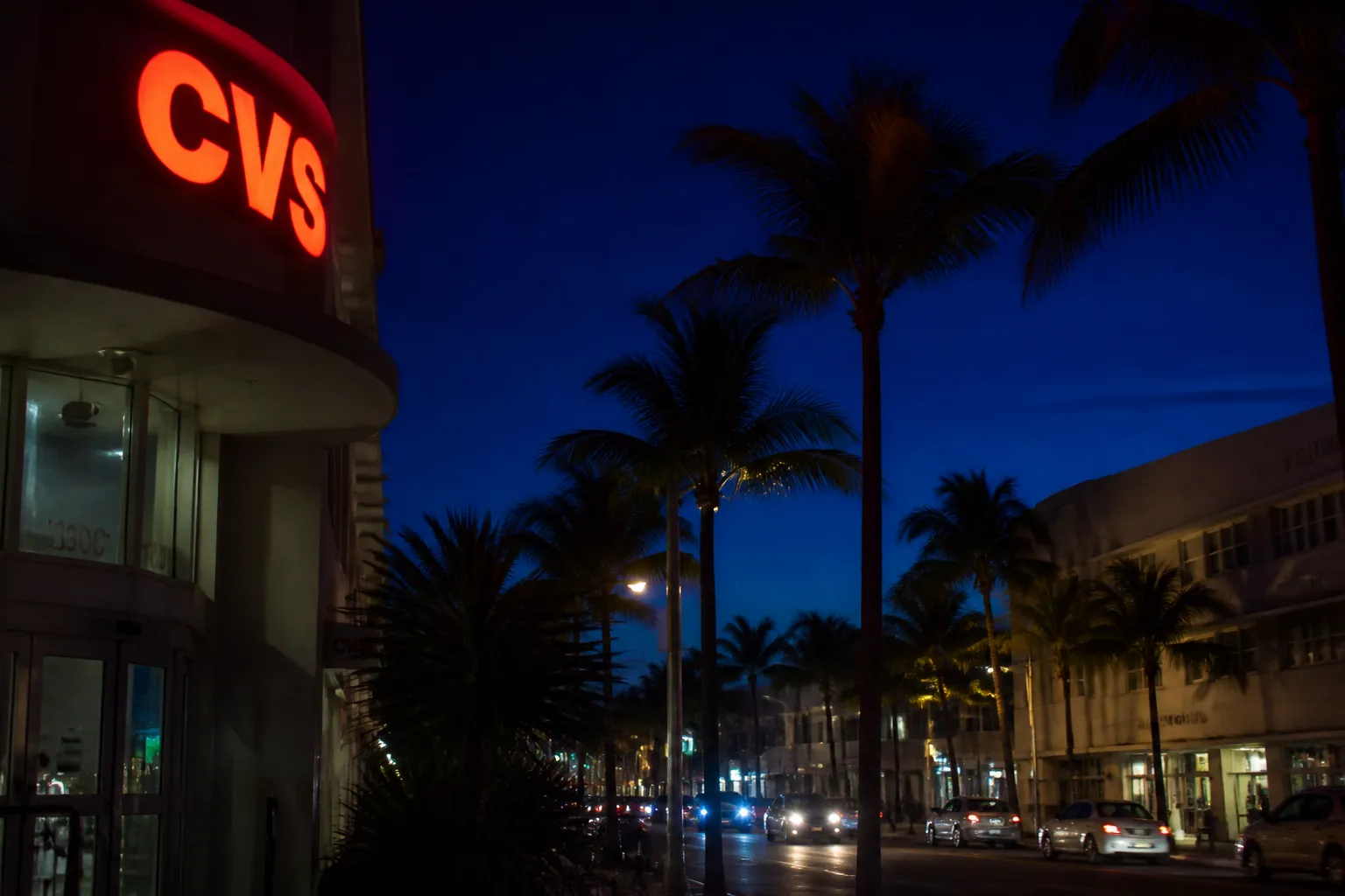 Neon red CVS sign glowing at night on a South Beach street lined with palm trees.