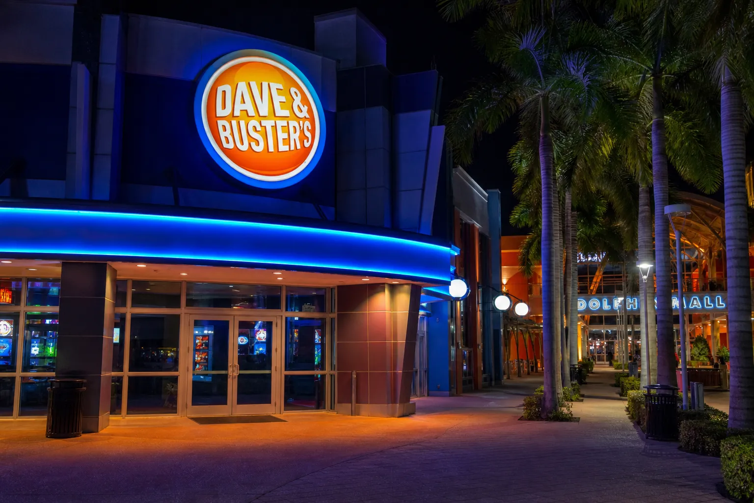 The illuminated exterior logo of Dave and Buster's at Miami's Dolphin Mall at night.