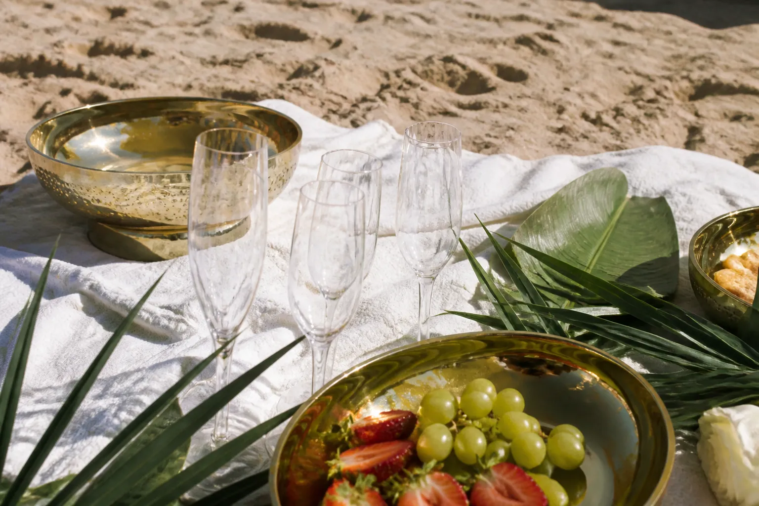 A stylish, budget-friendly beach picnic setup on the sand with plastic glassware and tropical leaf decorations.
