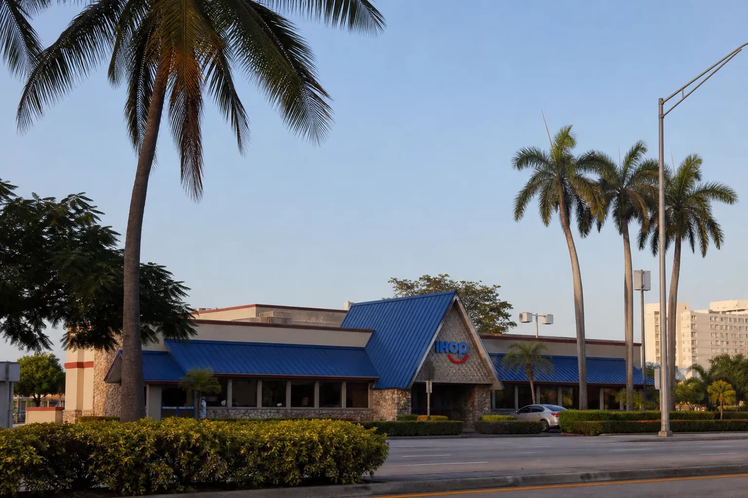 A wide shot of a classic diner building with palm trees under a bright blue Miami sky.