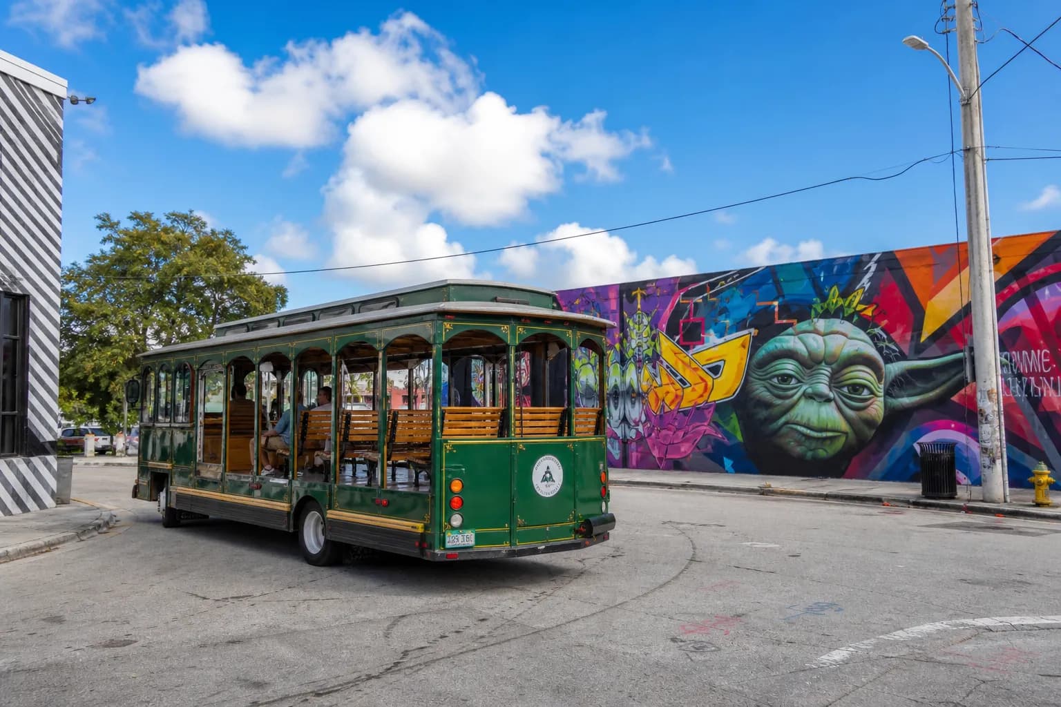 A Wynwood trolley driving past bright, graphic street art murals in Miami.