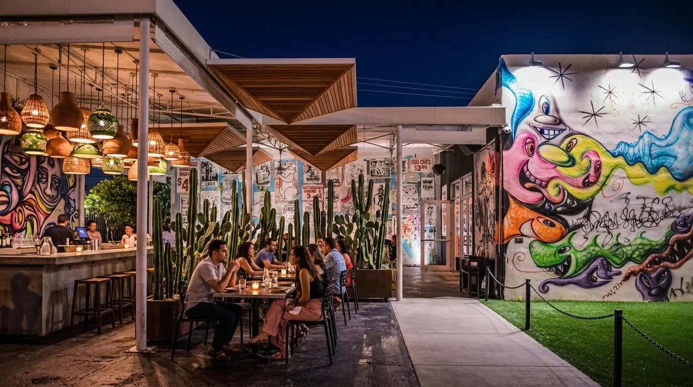 Night view of a Wynwood restaurant patio lit by hanging lights among cacti and wood canopies