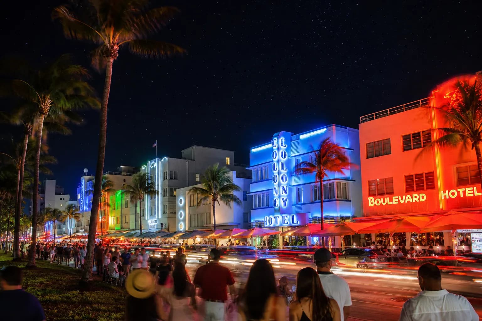 An aerial view of the neon-lit Ocean Drive in South Beach Miami during a festive night, with palm trees and ocean views