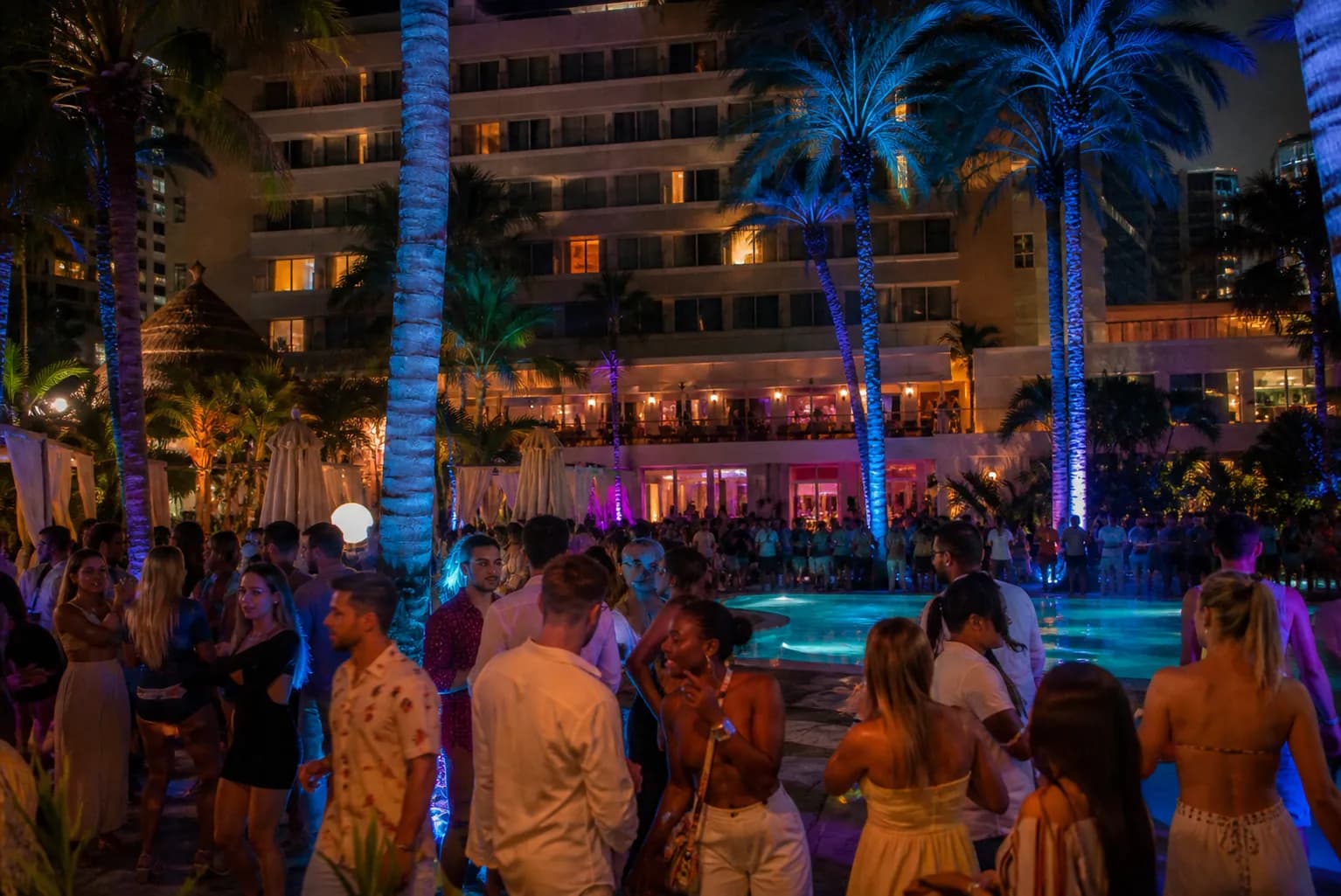 An illuminated luxury pool deck party in South Beach with purple and blue event lighting.