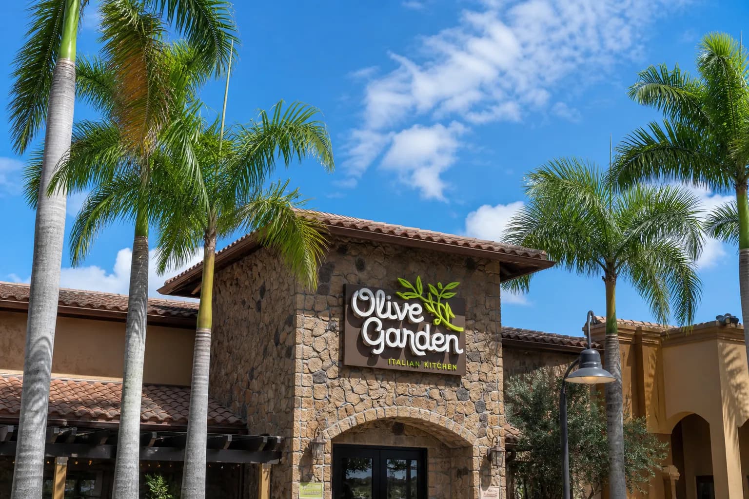 The exterior facade of the Doral Olive Garden restaurant building with palm trees