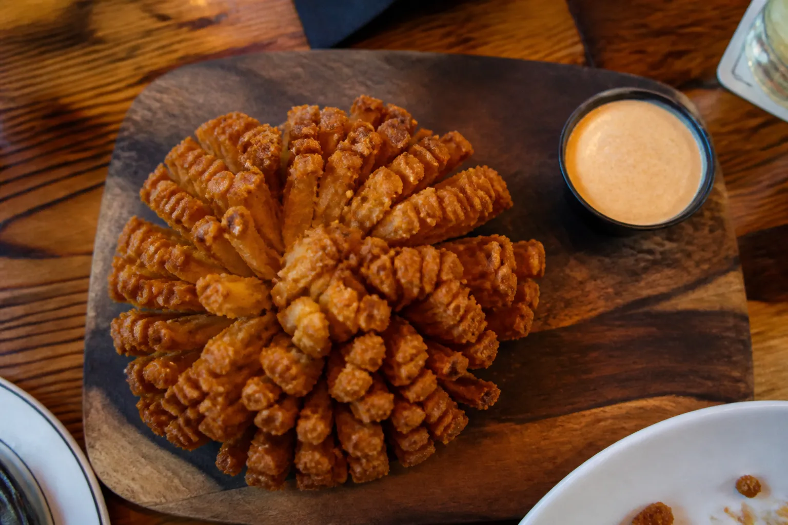 Crispy golden Bloomin Onion appetizer with dipping sauce on a wooden board