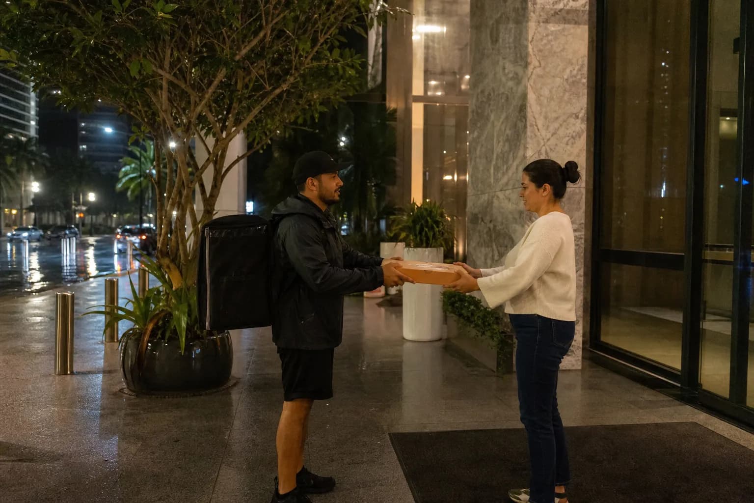 Delivery driver handing a pizza box to a customer outside a modern Brickell high-rise apartment building.