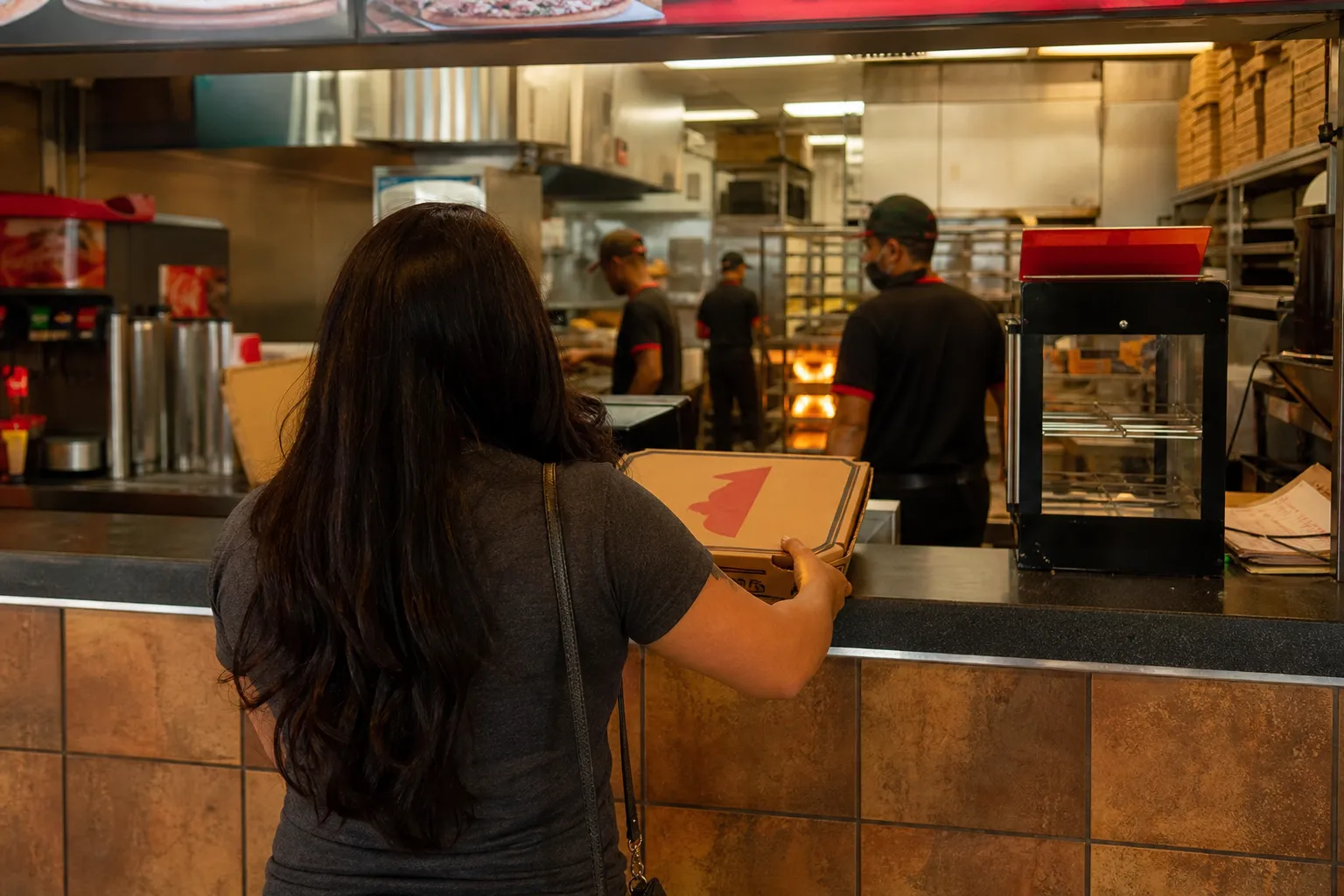 A customer receiving a hot pizza box at the pickup counter of a Miami location.