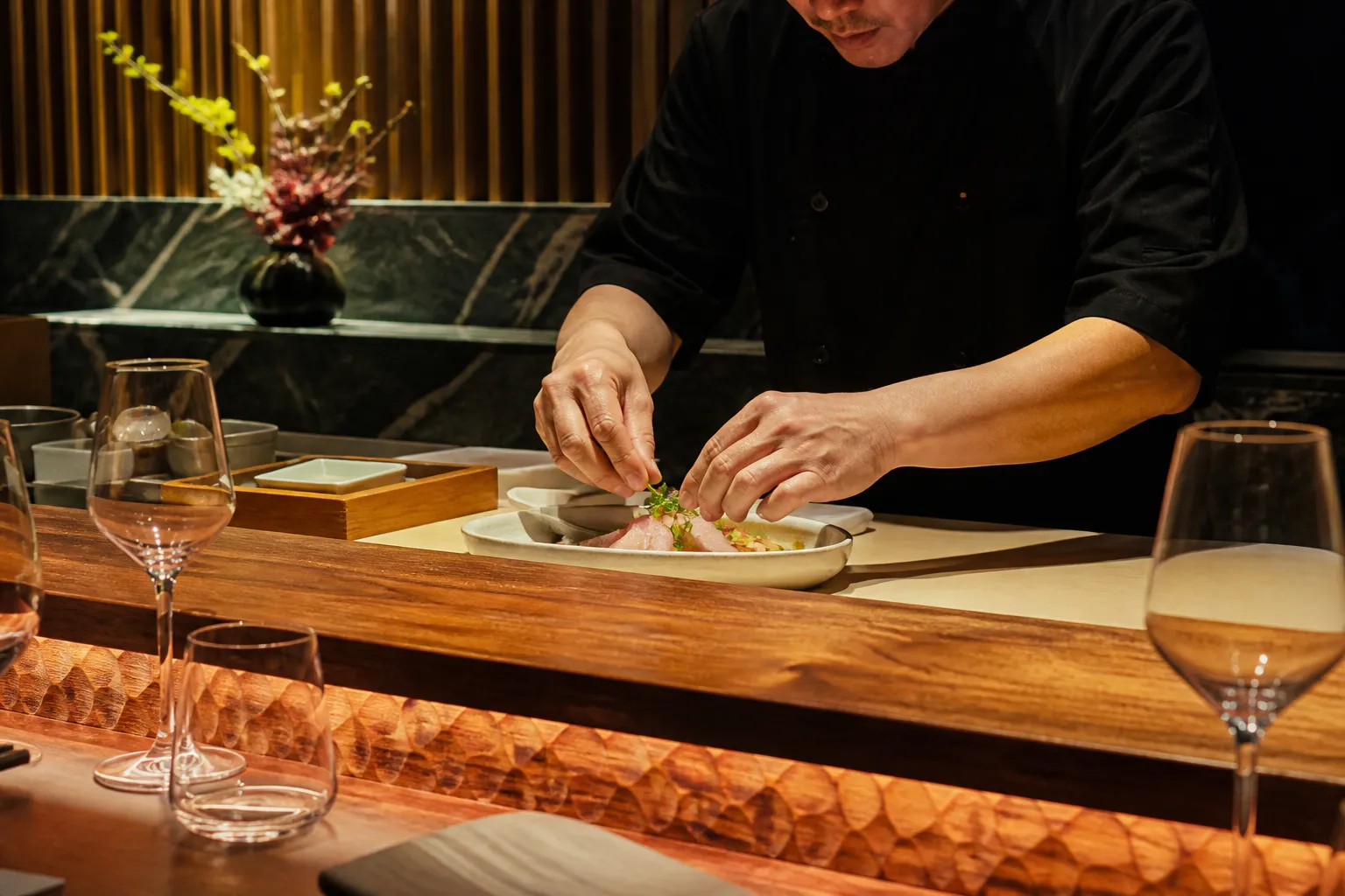 A chef plating a Nikkei dish at the sushi counter of Osaka in Brickell.