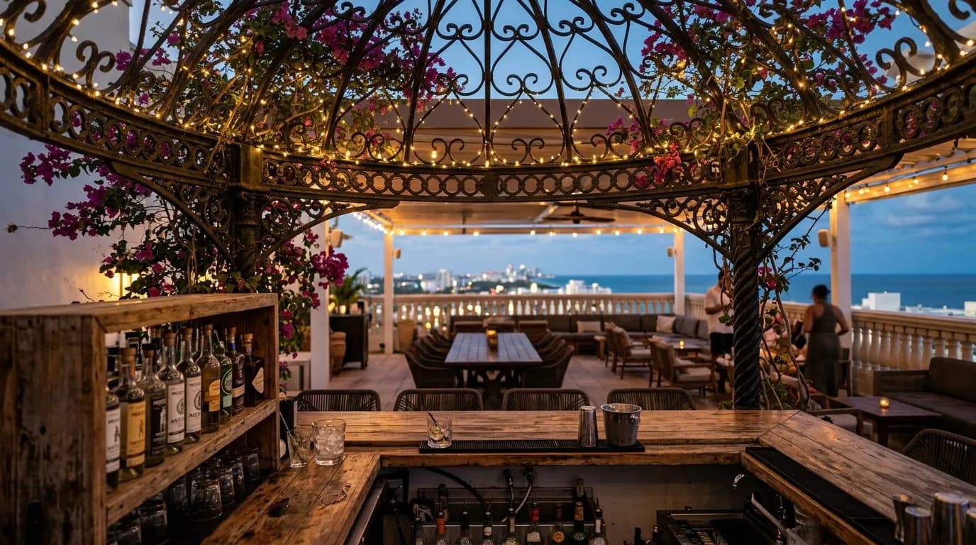 Bar counter under a cast-iron rooftop canopy strung with lights and bougainvillea