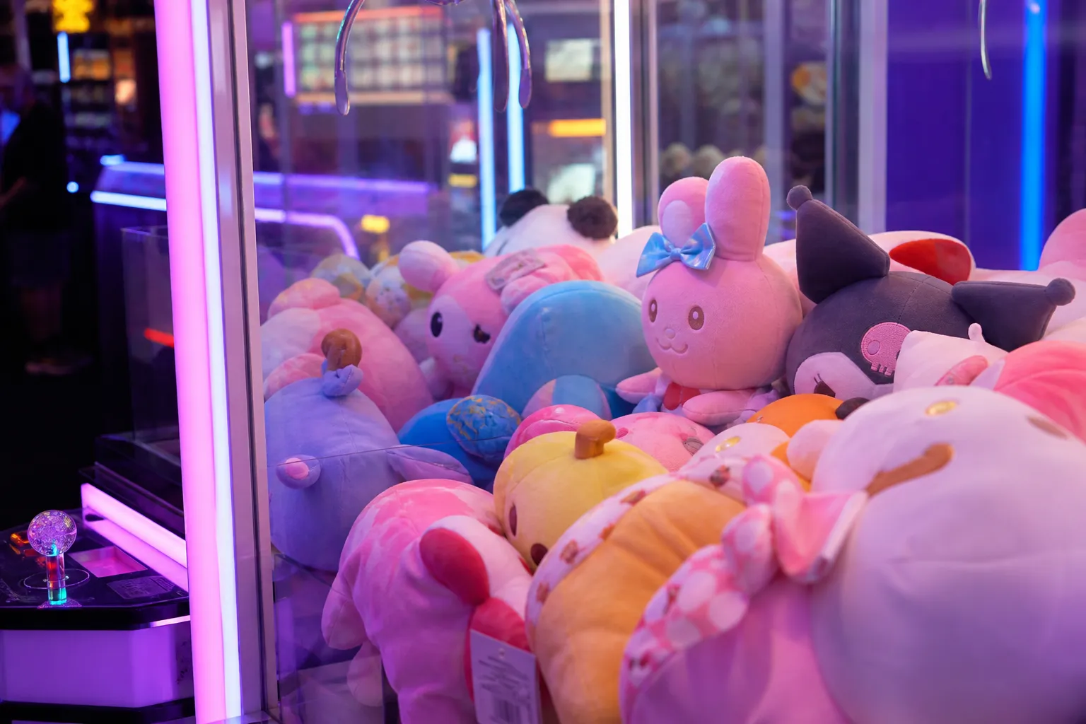 A close-up tabletop shot of a glossy e-amusement card and colorful arcade tokens resting on the vibrant, neon-lit control panel of a Japanese rhythm game cabinet.