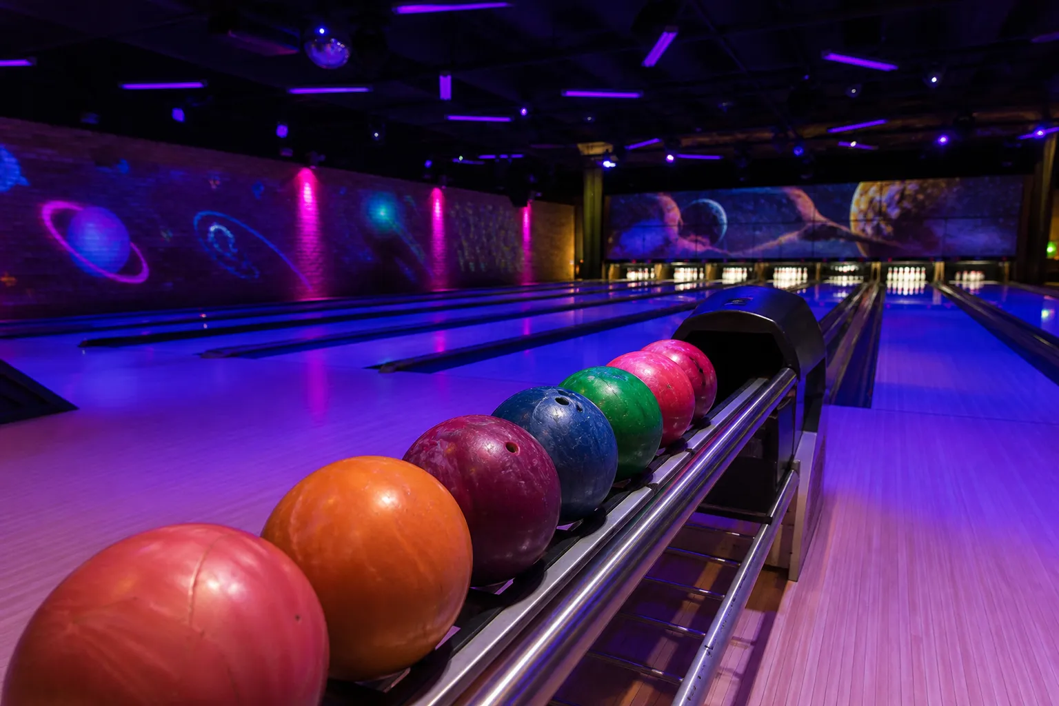 Cosmic bowling lanes glowing with blue and purple UV lights and aligned bowling balls.
