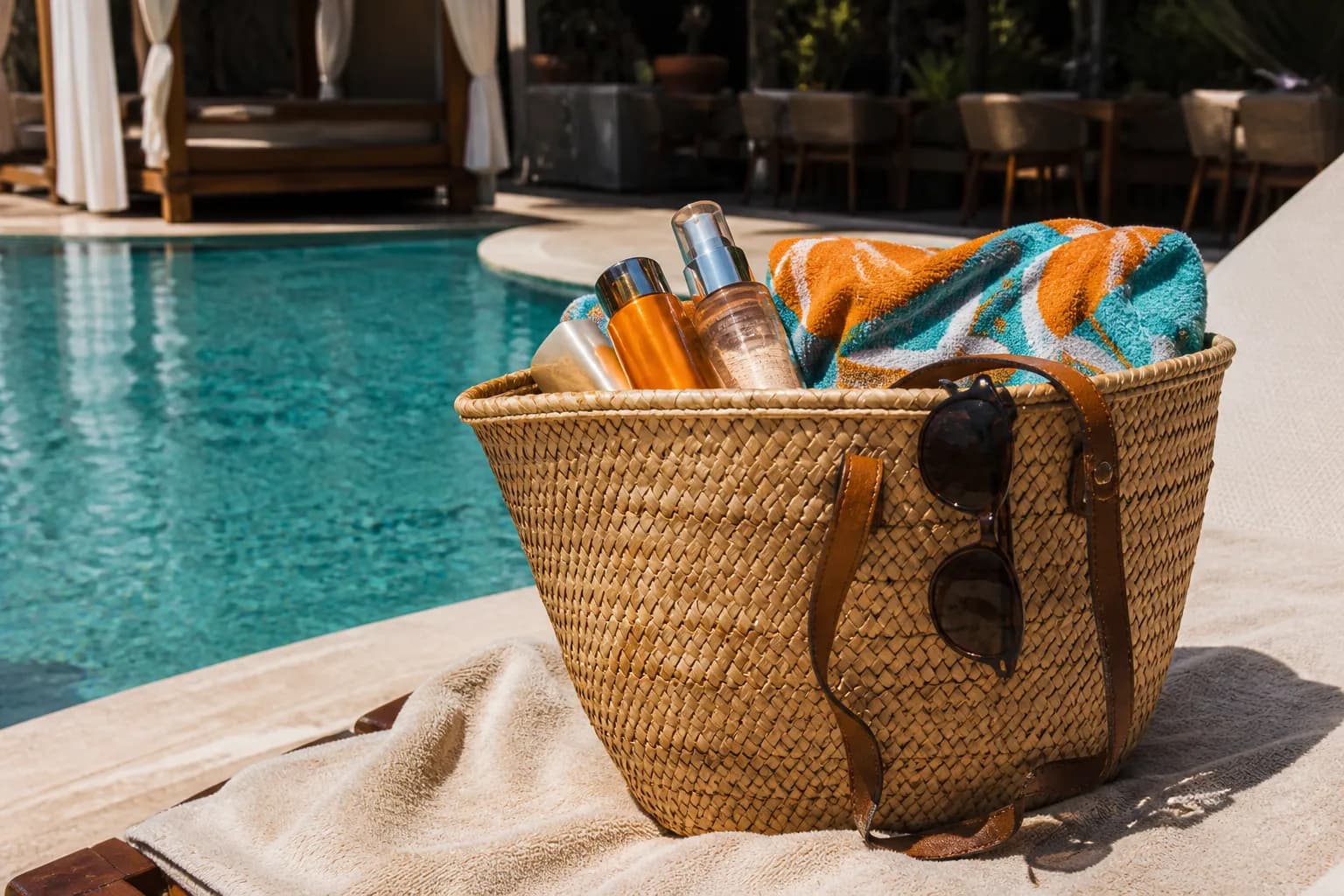 Straw beach bag with sunscreen and sunglasses on a lounge chair by a Miami pool.