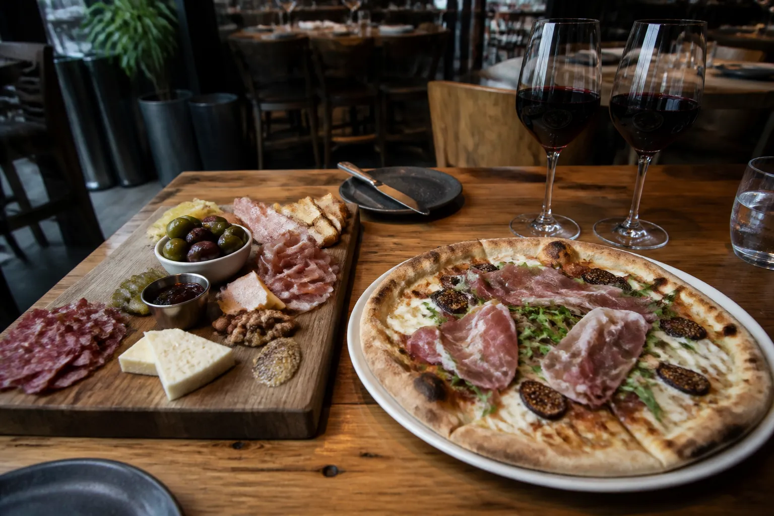 A fresh wood-fired pizza and charcuterie board paired with red wine on a wooden table.