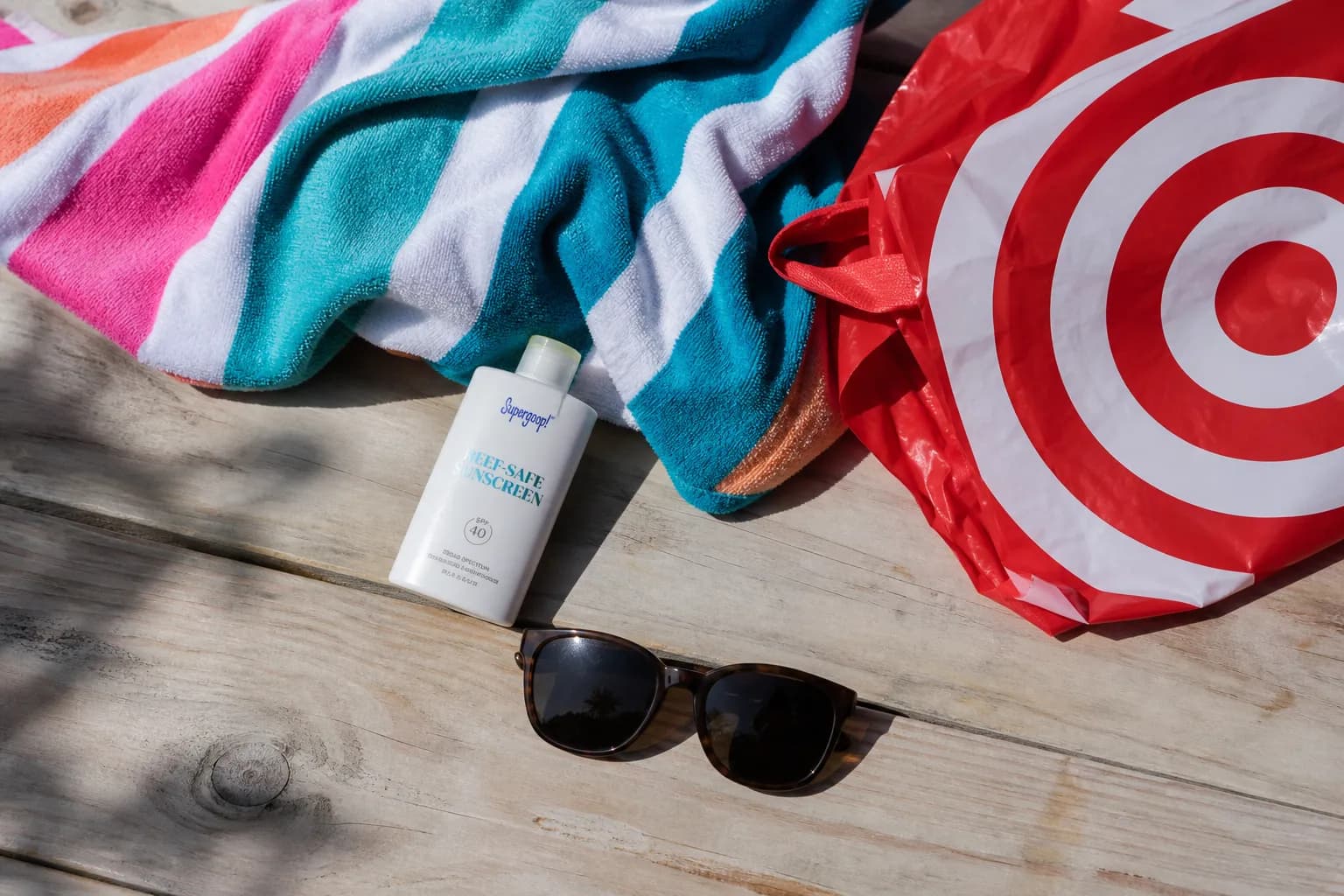 Beach gear including a towel, sunglasses, and sunscreen next to a red shopping bag.