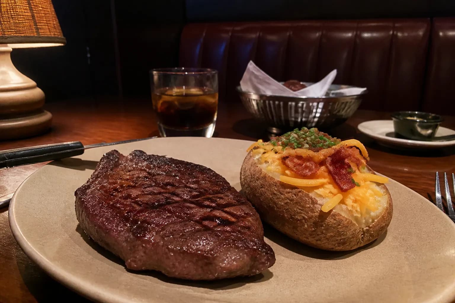 A grilled ribeye steak and loaded baked potato served in a cozy booth.