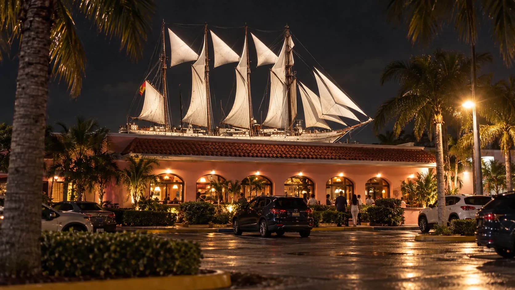 Low-angle night view of Islas Canarias in Westchester, with pink stucco walls, a red tile roof, palms and warm parking-lot lights.