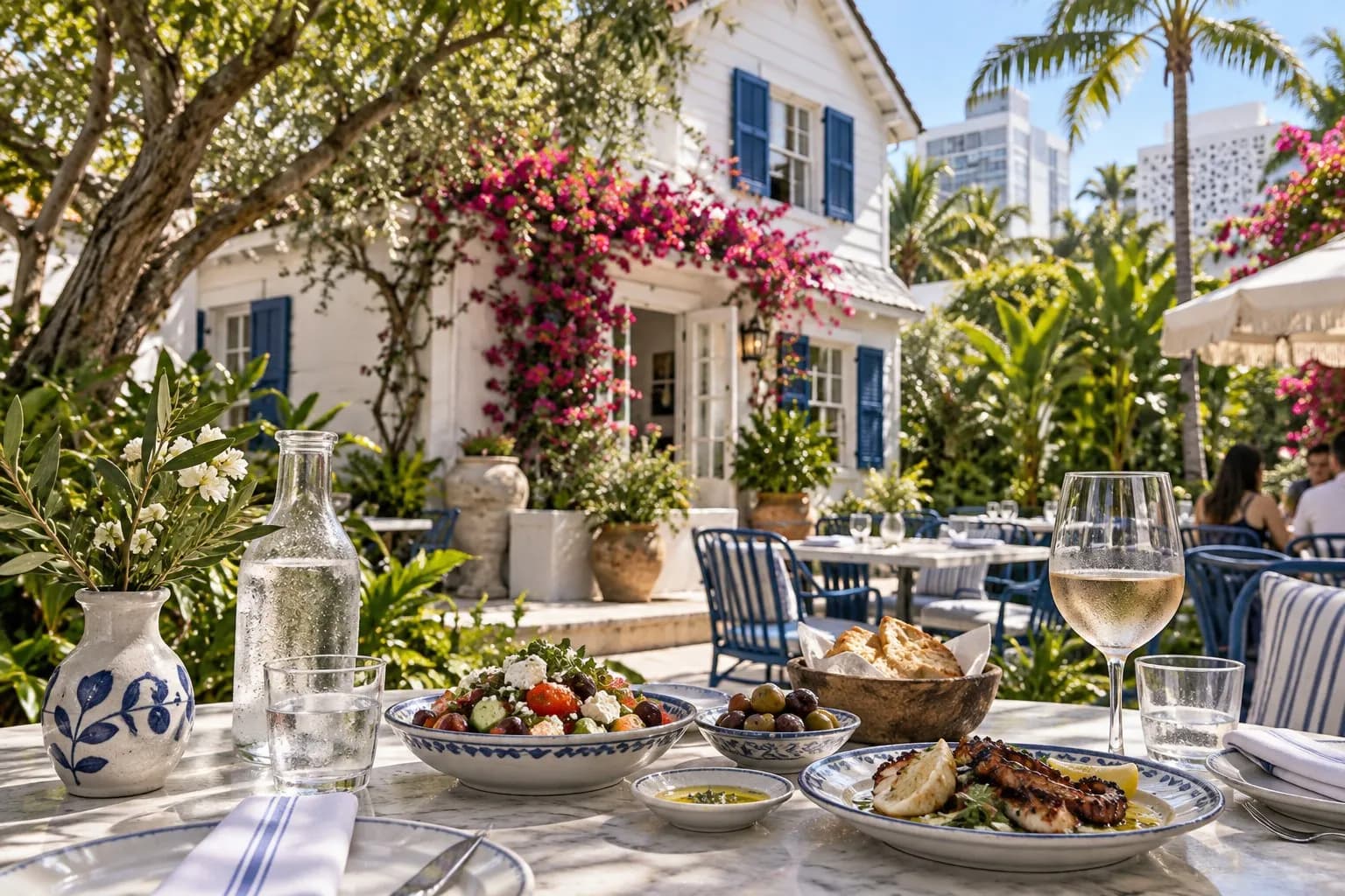 Mandolin Aegean Bistro garden patio with blue shutters, bougainvillea and shaded tables in daylight