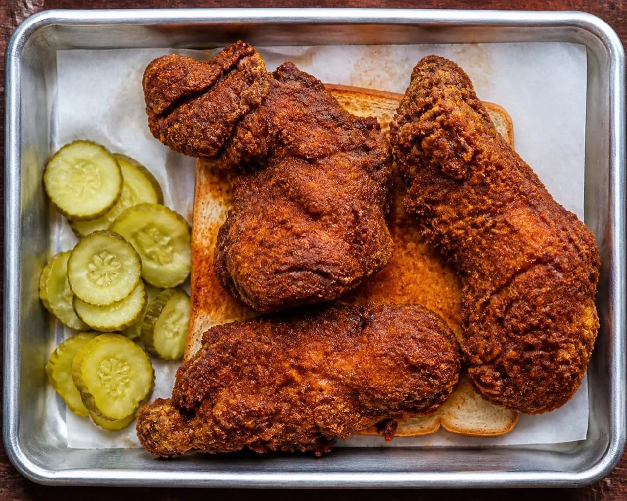 Fried chicken pieces on a plate with a slice of white bread and pickles