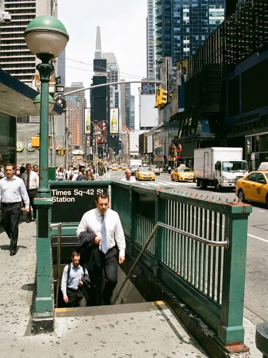 Office workers emerging from a green-railed Midtown Manhattan subway entrance at lunchtime with taxis passing on the avenue