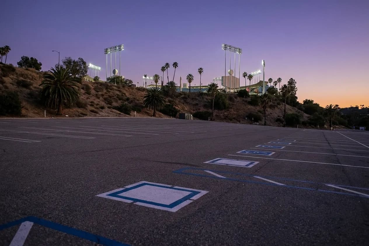 A hillside parking lot at dusk with stadium light towers rising behind it