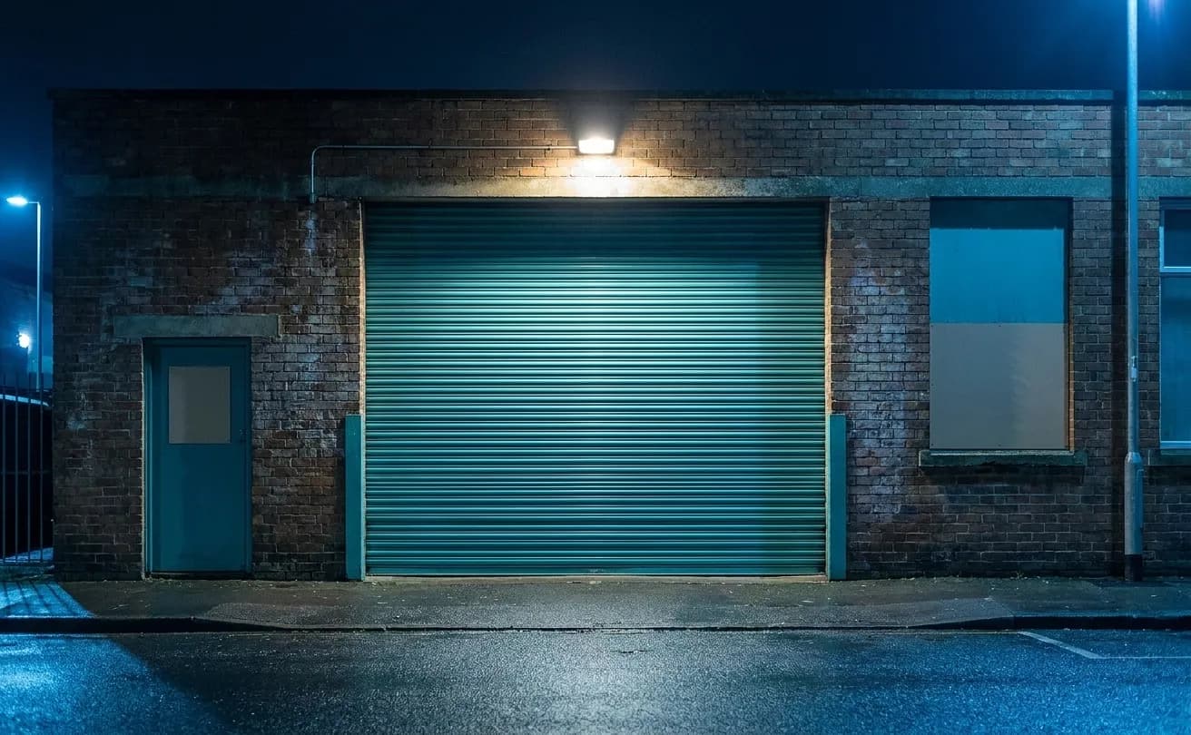 A metal roll-up door on a low brick industrial building at night