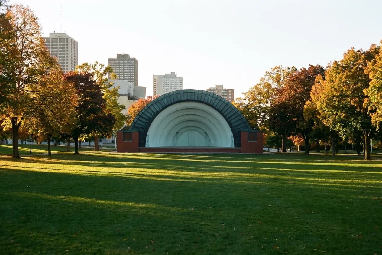 An open lawn in a city park with a covered bandshell at the far end