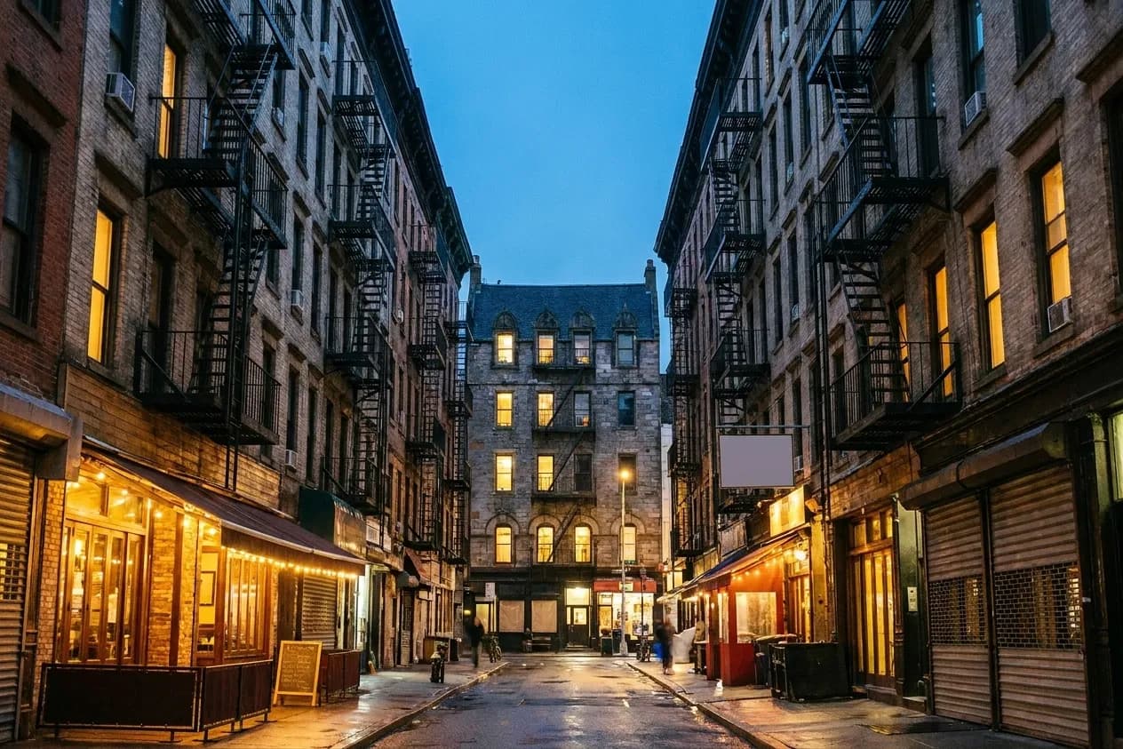 A narrow downtown street of tenement buildings with restaurant awnings at ground level
