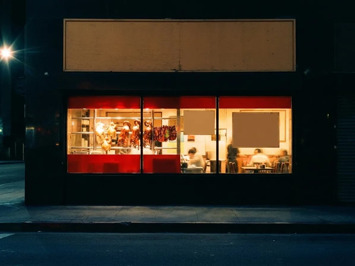 A lit restaurant window on a dark street with an empty pavement in front