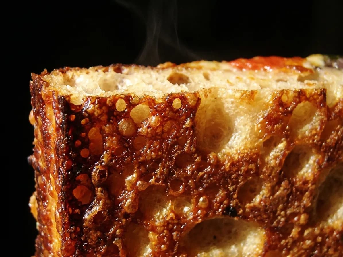 A close view of the crisp browned edge of a thick square pizza slice
