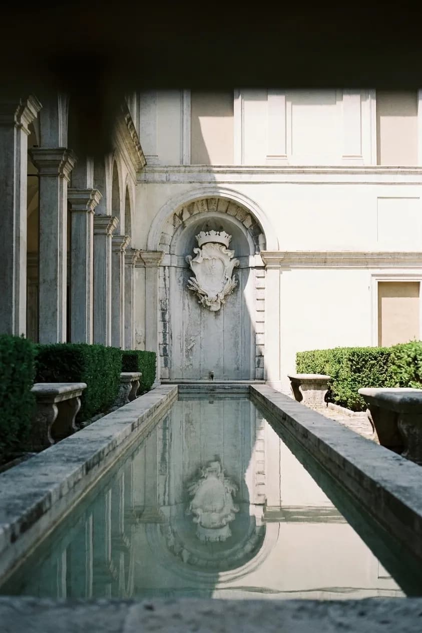 A wide shaded courtyard with a shallow water feature and stone benches