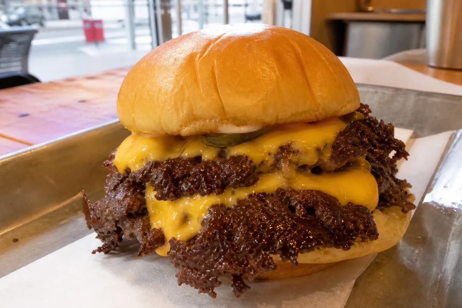 A close-up view of a freshly prepared double smashburger with crispy edges and melted cheese on a metal serving tray.