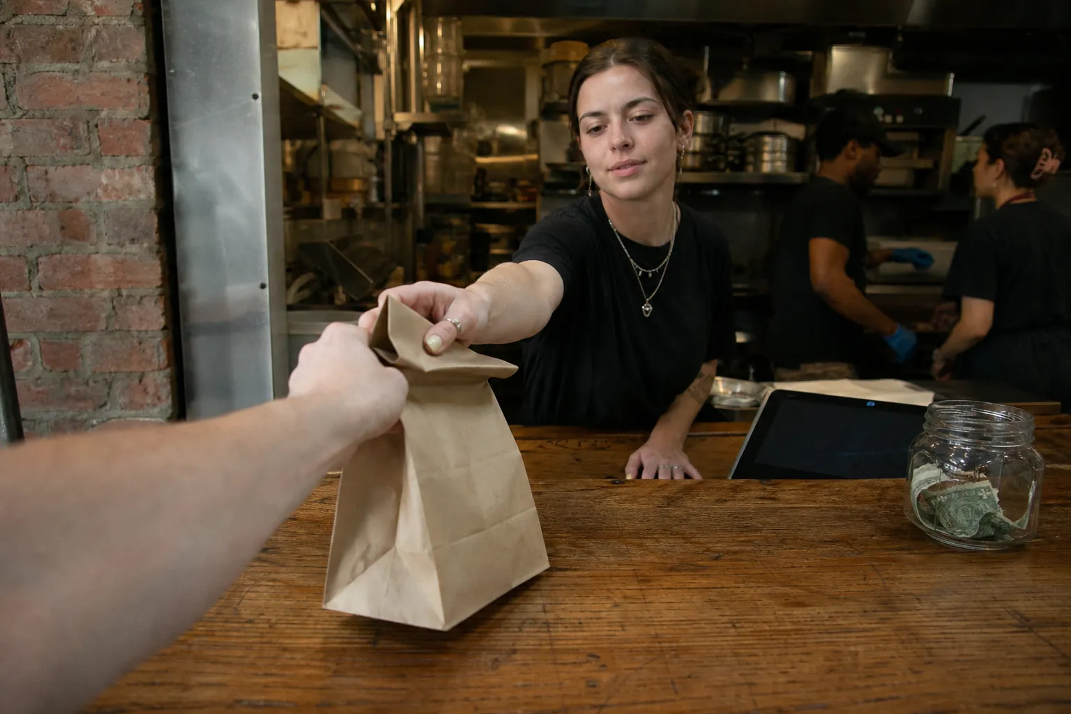 A view from the counter of the West Village 7th Street Burger location as a worker hands over a brown takeout bag.