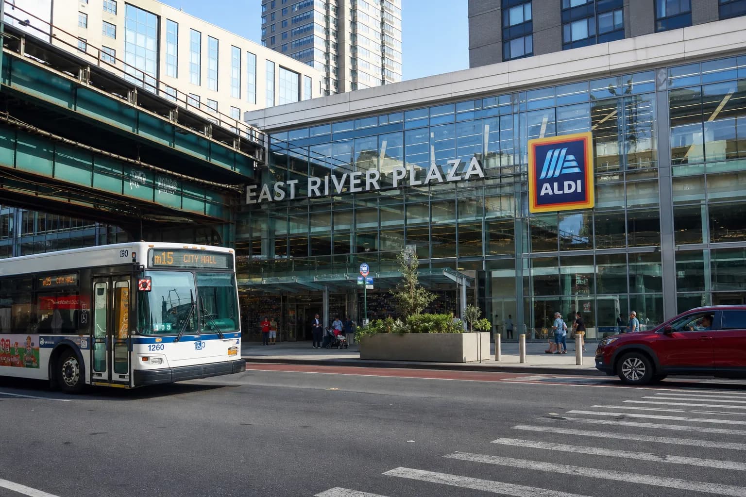 Modern multi-level retail plaza in NYC with a passing city bus and a visible Aldi sign.