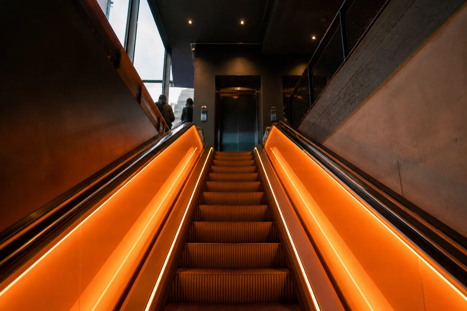 Glowing orange neon escalators leading up to the lobby entrance inside a modern boutique hotel in New York City