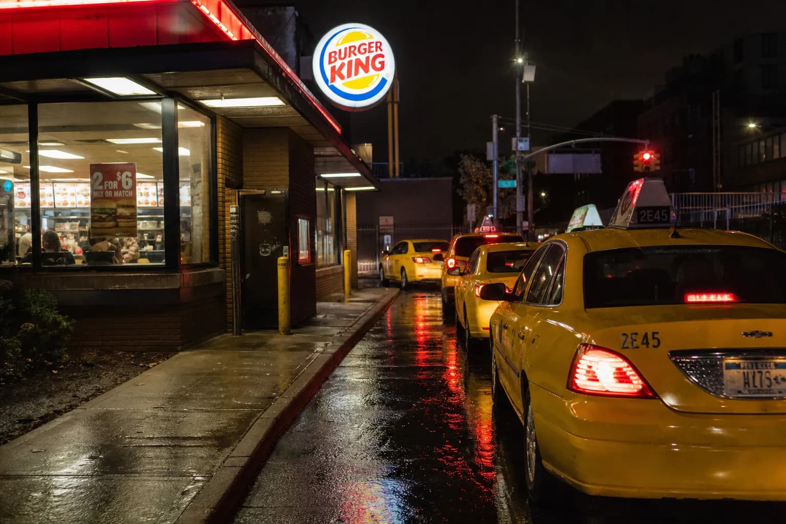 Wet pavement reflecting neon lights at a Brooklyn Burger King drive-thru at night.