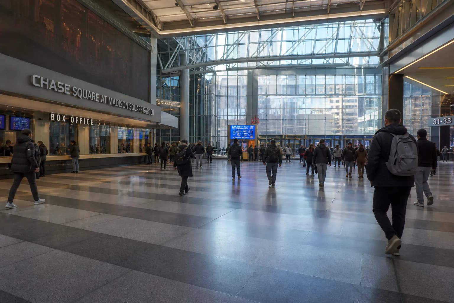 Wide-angle view of the modern, glass-canopied Chase Square lobby entrance of Madison Square Garden off 7th Avenue in New York City.